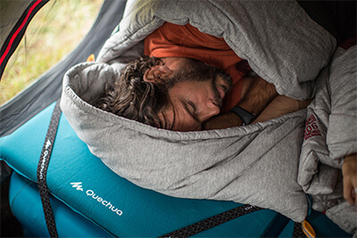 pessoa dormindo num saco de dormir com colchão e isolante térmico por baixo