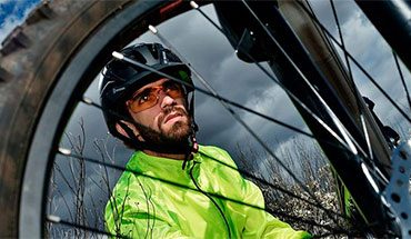 Homem com óculos de ciclismo agachado atrás dos aros do pneu da bike