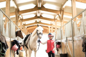 Uma criança fã de hipismo segurando a guia de seu cavalo dentro do estábulo